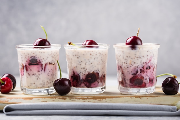 Chia pudding with cherry in a glass on a grey surface