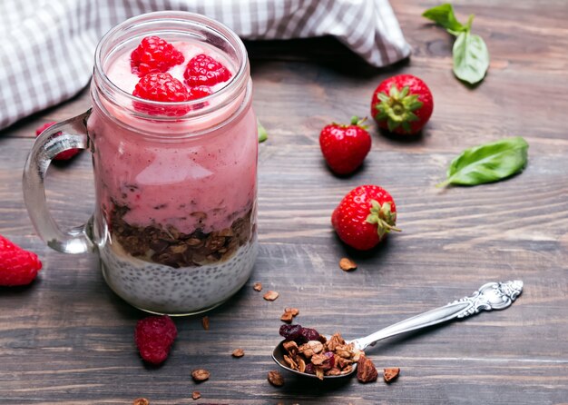 Chia pudding with granola and strawberries in a glass jar on the wooden table.