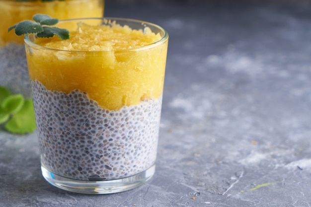 Chia pudding with mango and mint in glass on gray table