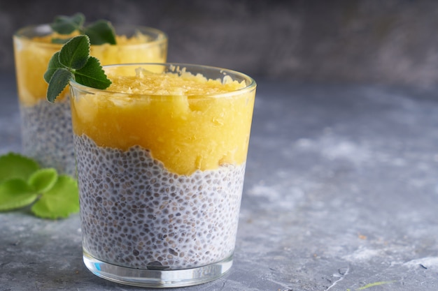 Chia pudding with mango and mint in glass on gray table