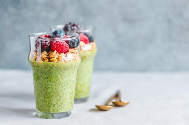 Chia pudding with matcha tea organic granola frozen berries in glasses Copy space