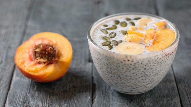 Chia seed pudding with peach and pumpkin seed on a dark wooden table.