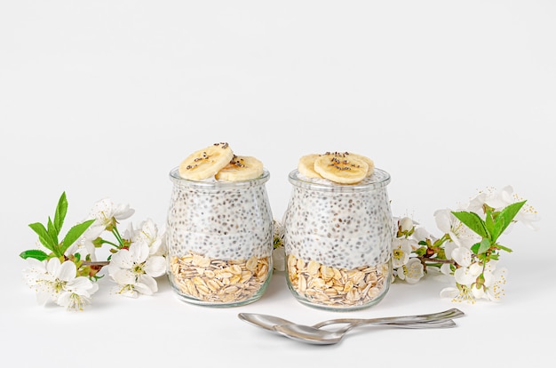 Chia seed pudding with yogurt and oats on white wall decorated with flowers. Superfood concept. Copy space