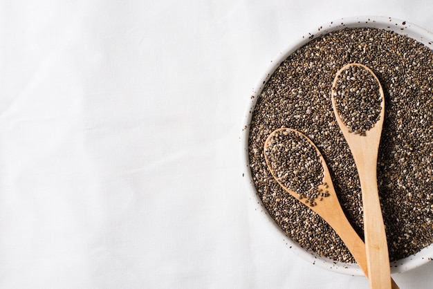 Chia seeds in bowl with two wooden spoon close up on white background