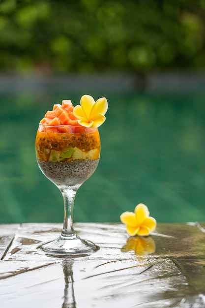 Chia seeds pudding with papaya passion fruit mango and avocado in a glass for breakfast on the background of the swimming pool water close up The concept of healthy eating superfood