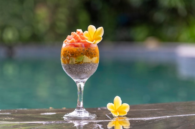 Chia seeds pudding with papaya passion fruit mango and avocado in a glass for breakfast on the background of the swimming pool water closeup The concept of healthy eating superfood