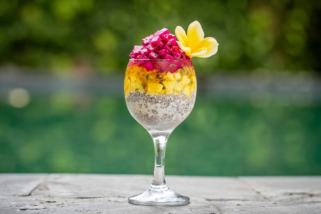 Chia seeds pudding with red dragon fruit passion fruit mango and avocado in a glass for breakfast on the background of the swimming pool water closeup The concept of healthy eating