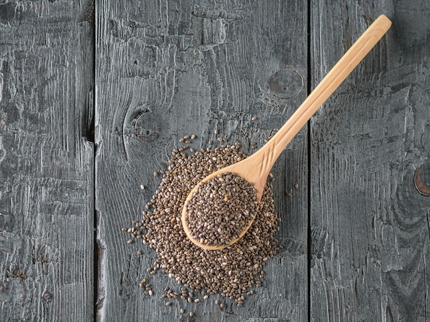 Photo chia seeds in a spoon on a dark wooden table. the view from the top. flat lay.