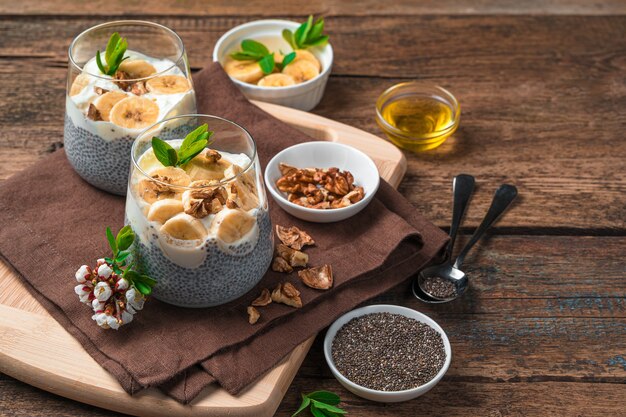 Chia seeds with oat milk, cream, banana, honey and nuts on a brown wall. Healthy, natural dessert. Top view with copy space.