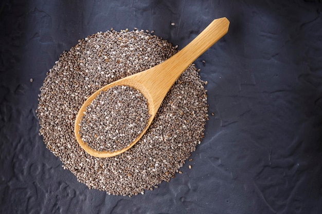 Chia seeds and wooden spoon on black background