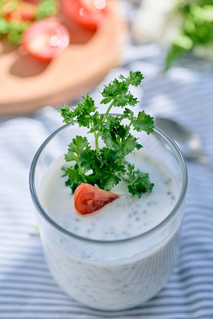 Chia seeds and yogurt in a glass with greens and tomatoes