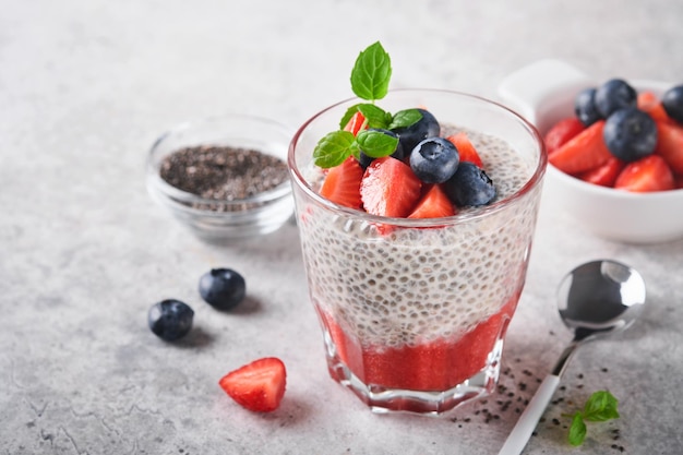 Budino di chia alla fragola sana colazione vegana budino di semi di chia con frutti di bosco freschi e menta in vetro su sfondo grigio cemento concetto di alimentazione sana dieta menu fitness messa a fuoco selettiva