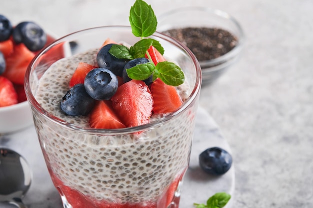 Chia strawberry pudding Healthy vegan breakfast chia seeds pudding with fresh berries and mint in glass on gray concrete background Concept of healthy eating dieting fitness menu Selective focus