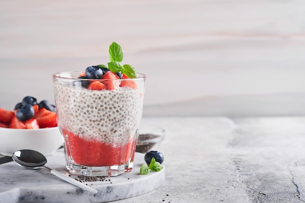 Budino di chia alla fragola sana colazione vegana budino di semi di chia con frutti di bosco freschi e menta in vetro su sfondo grigio cemento concetto di alimentazione sana dieta menu fitness messa a fuoco selettiva