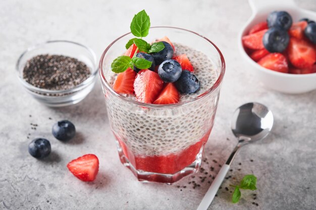 Chia strawberry pudding Healthy vegan breakfast chia seeds pudding with fresh berries and mint in glass on gray concrete background Concept of healthy eating dieting fitness menu Selective focus