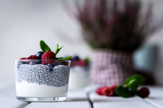 Chia with wild berries. Raspberries and blueberries. Delicious and healthy dessert and violet flowers  over a white wood rustic table.