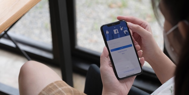 CHIANG MAI ,THAILAND NOV 14 2021 : Woman holding a iPhone X with social Internet service Facebook on the screen.