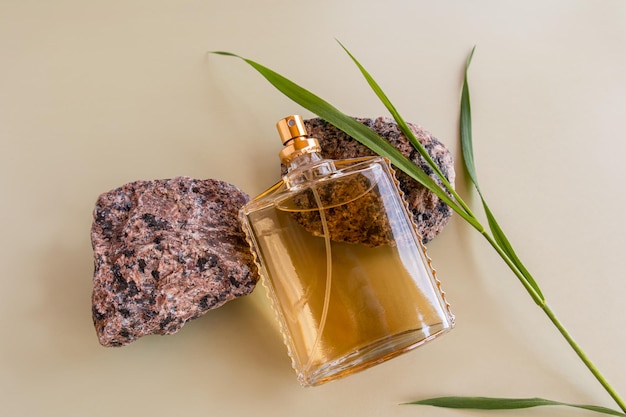 A chic bottle of men's perfume or toilet water on granite stones and a green blade of grass foreground pastel background