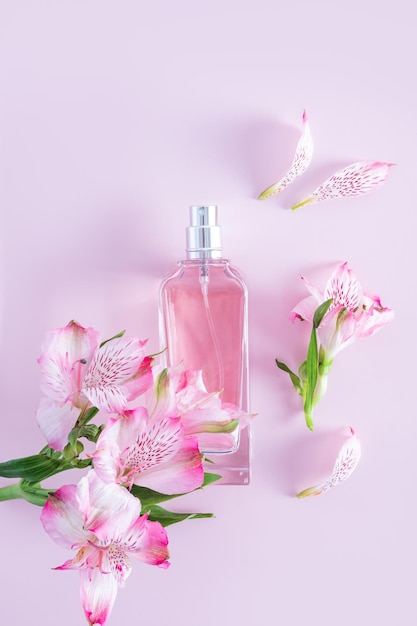 A chic bottle of women's perfume or cosmetic spray on a pink vertical background among the delicate flowers of astromeria aroma presentation