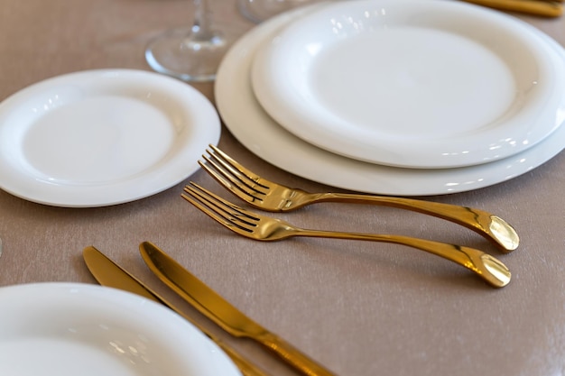 Шикарные и элегантные позолоченные столовые приборы и белые тарелки, сервировка стола с пустыми тарелками