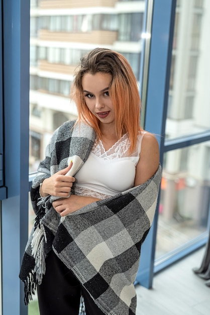 Chic portrait of a pretty girl with a beautiful hairstyle and perfect makeup near a spacious window The concept of a girl by the window