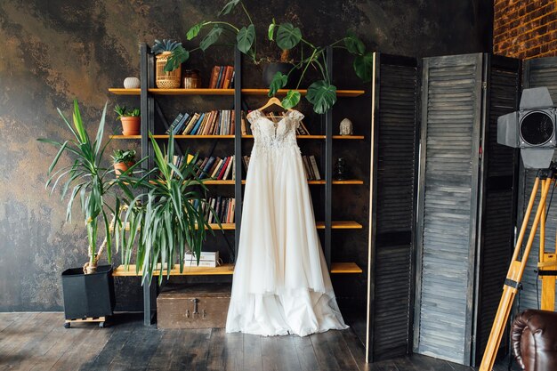 A chic silk wedding dress hangs on a bookcase.