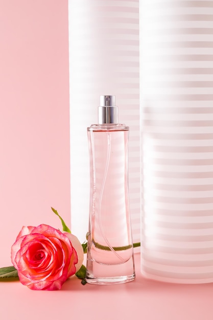 A chic tall bottle of women's perfume or eau de toilette on a decorative white pink background with a rose Vertical view