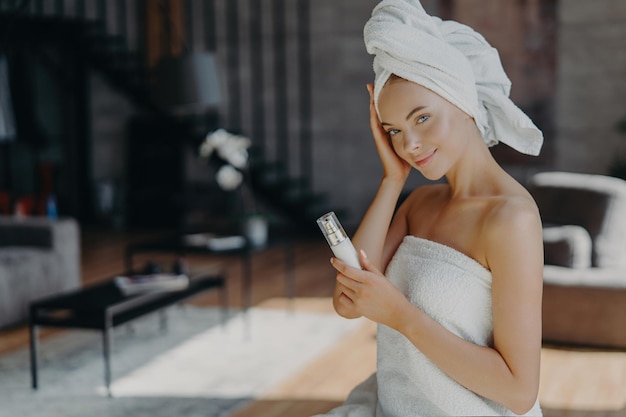 Chic woman with towel on hair holding a lotion tube in a stylish interior