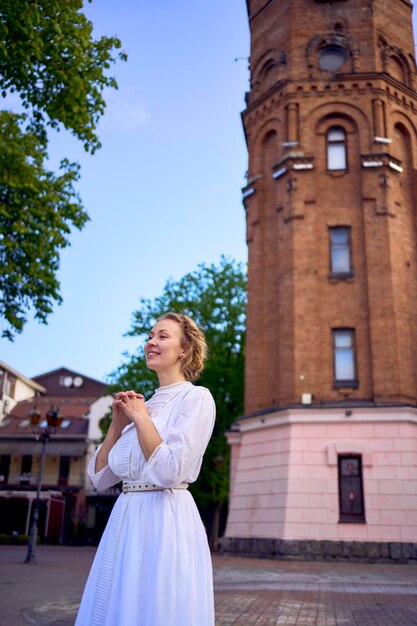 chic young woman in a white vintage dress on the square near the historic water tower in Vinnytsia