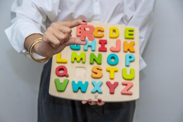 Chica joven sostiene letra "R" mostrando bloques de aprendizaje del alfabeto bÃÂ¡sico para niÃÂ±os.