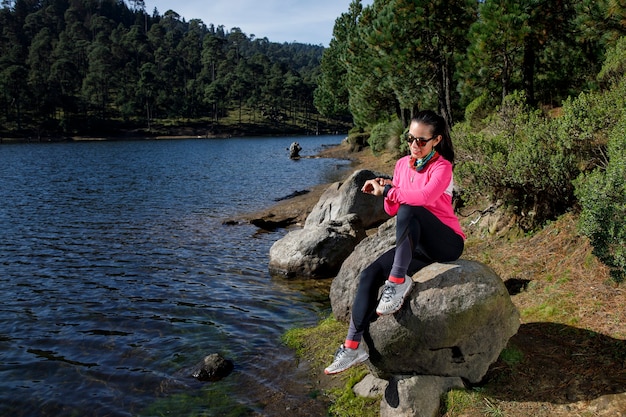 Chica revisando su reloj inteligente a la orilla de un lago despues de correr