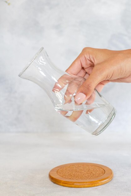 Chica sostiene vaso de cristal con agua para servir en la mesa, fondo blanco aislado con textura