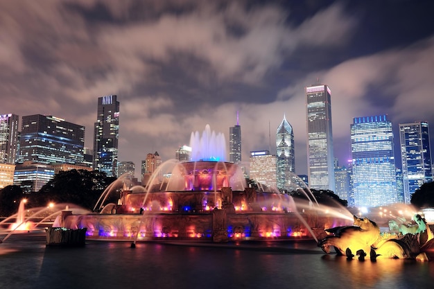Горизонт Чикаго с небоскребами и Букингемским фонтаном в Грант-парке ночью, освещенный разноцветными огнями.