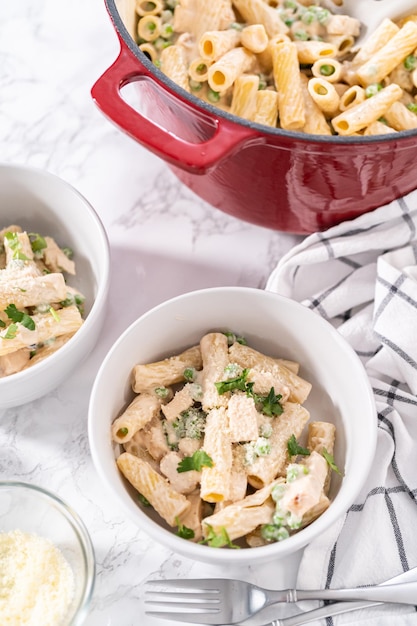 Chicken alfredo pasta with green peas and rigatoni pasta in a small bowl.