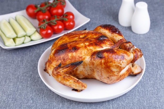 맛있는 빵 껍질에 통째로 구운 치킨 전통 요리 배경에는 하얀 접시에 오이와 체리 토마토가 있습니다. 근접 촬영 선택적 초점 회색 배경