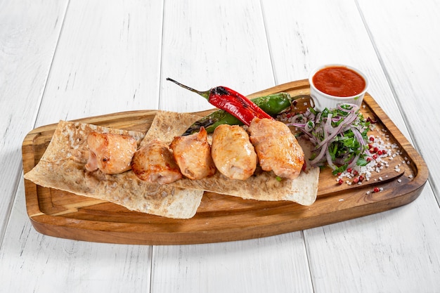 Chicken barbeque with grilled vegetables and red sauce on wooden desk