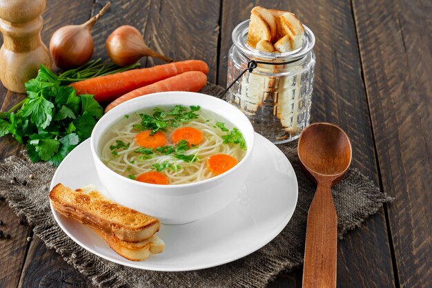 Chicken bouillon with noodles and carrot slices on a wooden\
table in rustic style.