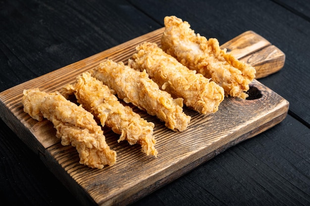 Chicken breaded fillet stripes on black wooden table.