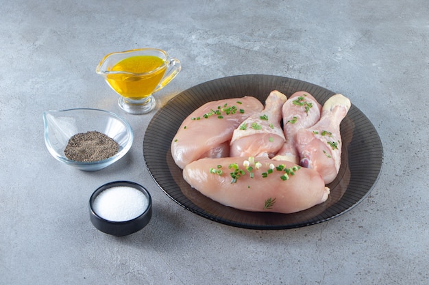Petto di pollo e cosce su un piatto accanto a ciotole di spezie, sulla superficie di marmo.