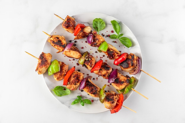 Foto filetto di petto di pollo alla griglia spiedini di barbecue con verdure e basilico in un piatto sul tavolo bianco