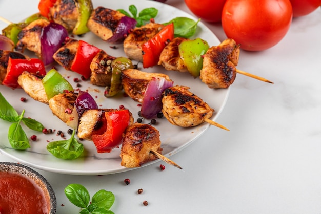 Photo chicken breast fillet grilled barbecue skewers with vegetables, basil and tomato ketchup in a plate on white table