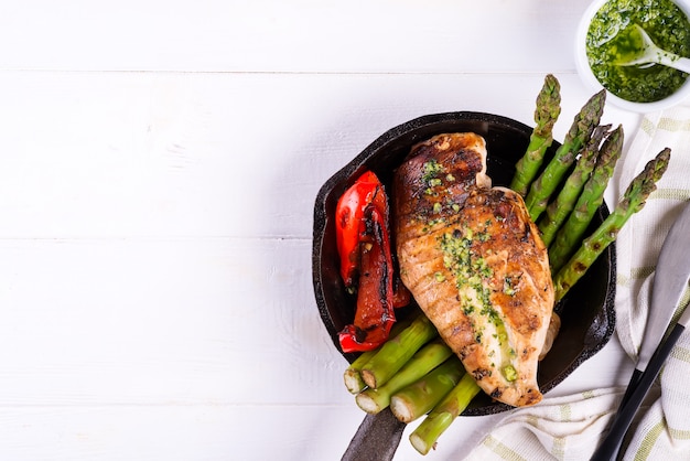 Chicken breast grill with bbq vegetables and pesto sauce in a cast iron pan on white 