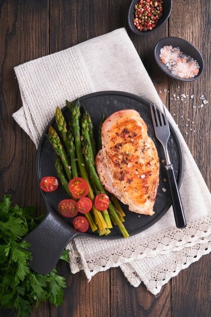 Chicken breast grilled with vegetables Grilled chicken steak asparagus and cherry tomatoes in black plate on wooden dark table background Healthy diet lunch Barbecue steak fried Top view