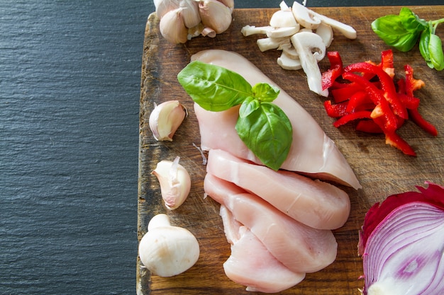 Chicken breast and ingredients on dark stone background