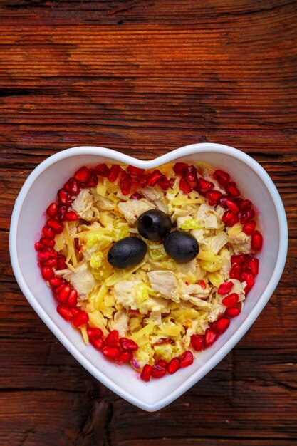 Chicken breast puff salad garnished with pomegranate and olives in a salad bowl on the table.