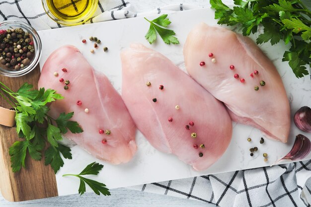 Chicken breast Two Chicken fillet with spices olive oil and parsley on white stone cutting board on white wooden table background Top view with copy space Food meat cooking background