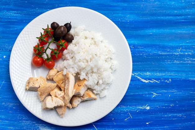 Chicken breast with boiled rice and tomato on white plate