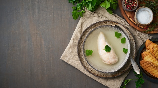 Chicken broth with chicken fillet, parsley and toast on dark brown background, top view, copy space