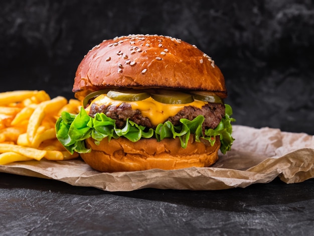 暗い背景にチェダーチーズとフライドポテトを添えたチキンバーガー