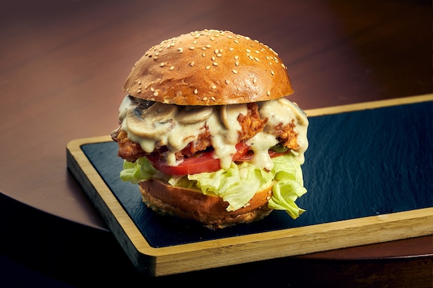 Chicken burger with cheese, tomato, onion and mushrooms on a black board. Fast food